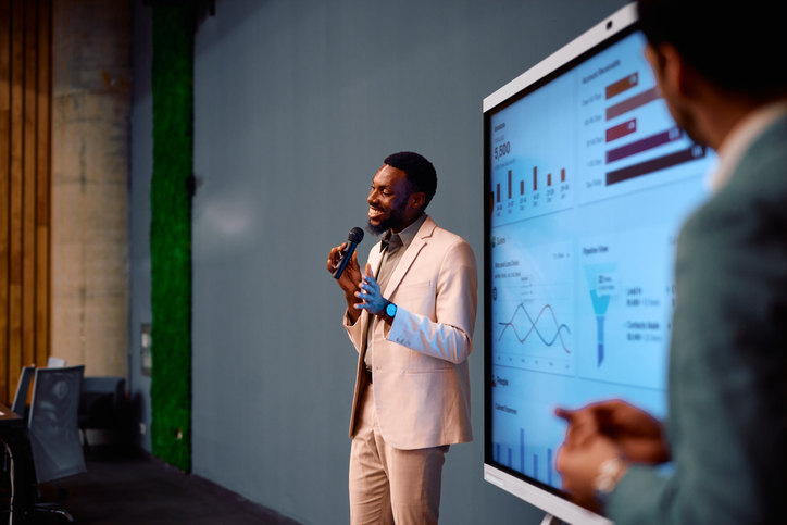 Confident young businessman giving a presentation using a microphone and interactive whiteboard